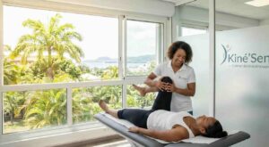 Séance de kinésithérapie au cabinet Kiné'Sens à Fort-de-France, Martinique. Un kiné manipule la jambe d'une patiente sur une table de soin avec vue sur la baie.